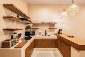 A modern kitchen with wooden shelves, a built-in toaster, a coffee maker, and pendant lighting.