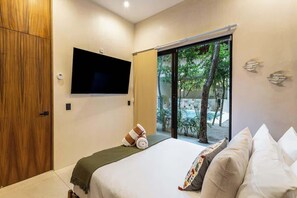 A bedroom with a bed, a TV mounted on the wall, a window with a view of trees, and a sliding door.