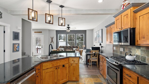 A spacious kitchen with wooden cabinets, a dishwasher, a stove, and a large island with seating. - Schweitzer Mountain 3 bd Getaway (Sandpoint)