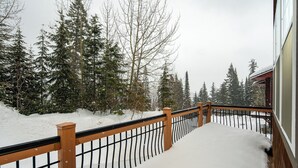 A snow-covered deck with a wooden railing and metal balusters, surrounded by snow-laden trees. - Schweitzer Mountain 3 bd Getaway (Sandpoint)