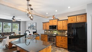 A modern kitchen with wooden cabinets, a black refrigerator, and a central island with bar stools. - Schweitzer Mountain 3 bd Getaway (Sandpoint)