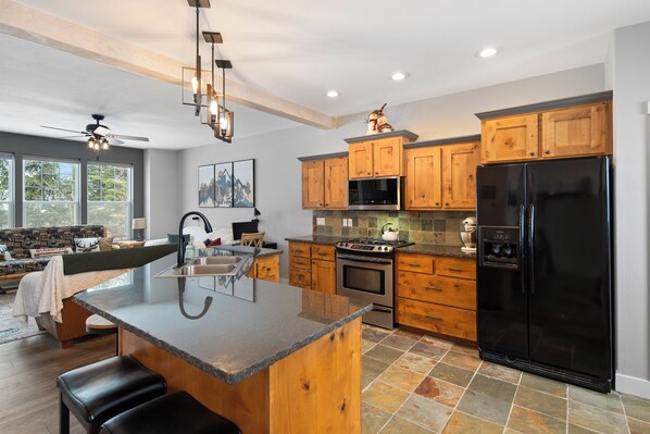 A modern kitchen with wooden cabinets, a black refrigerator, and a central island with bar stools. - Schweitzer Mountain 3 bd Getaway (Sandpoint)