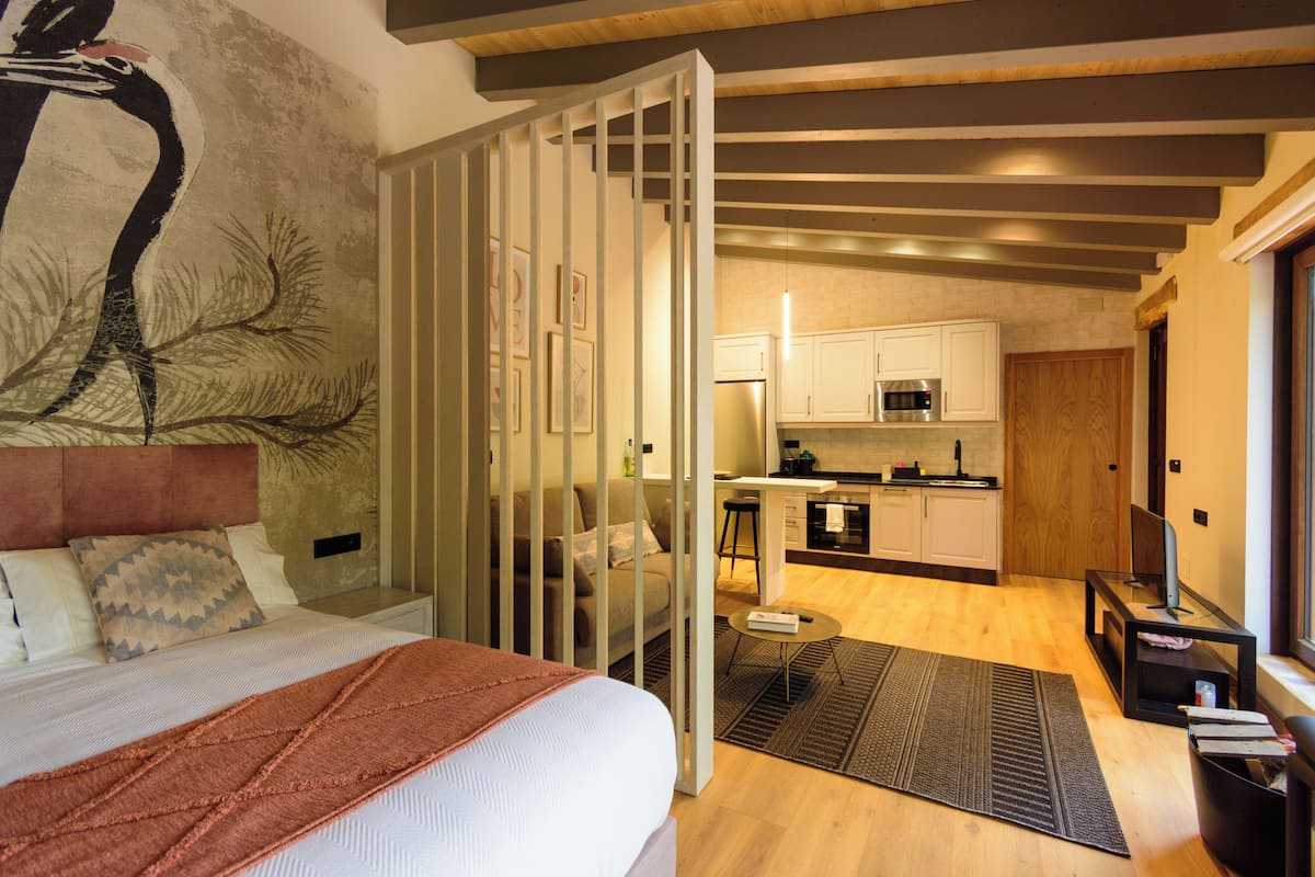 A modern hotel room with a bed, a large artwork, a kitchen area, and a seating area.