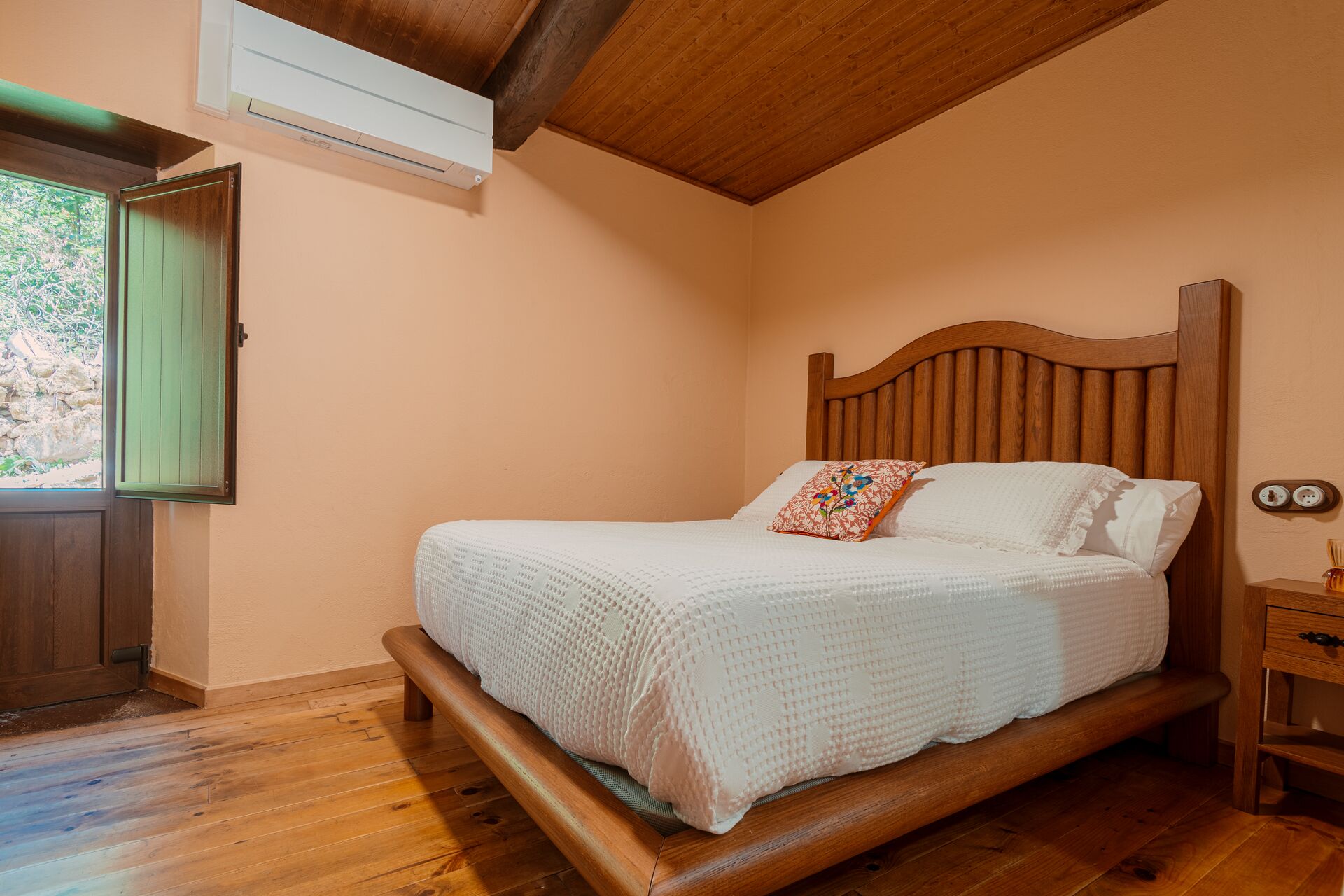 A bedroom with a wooden bed, a green door, and a window with a view of greenery.