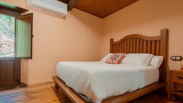 A bedroom with a wooden bed, a green door, and a window with a view of greenery.