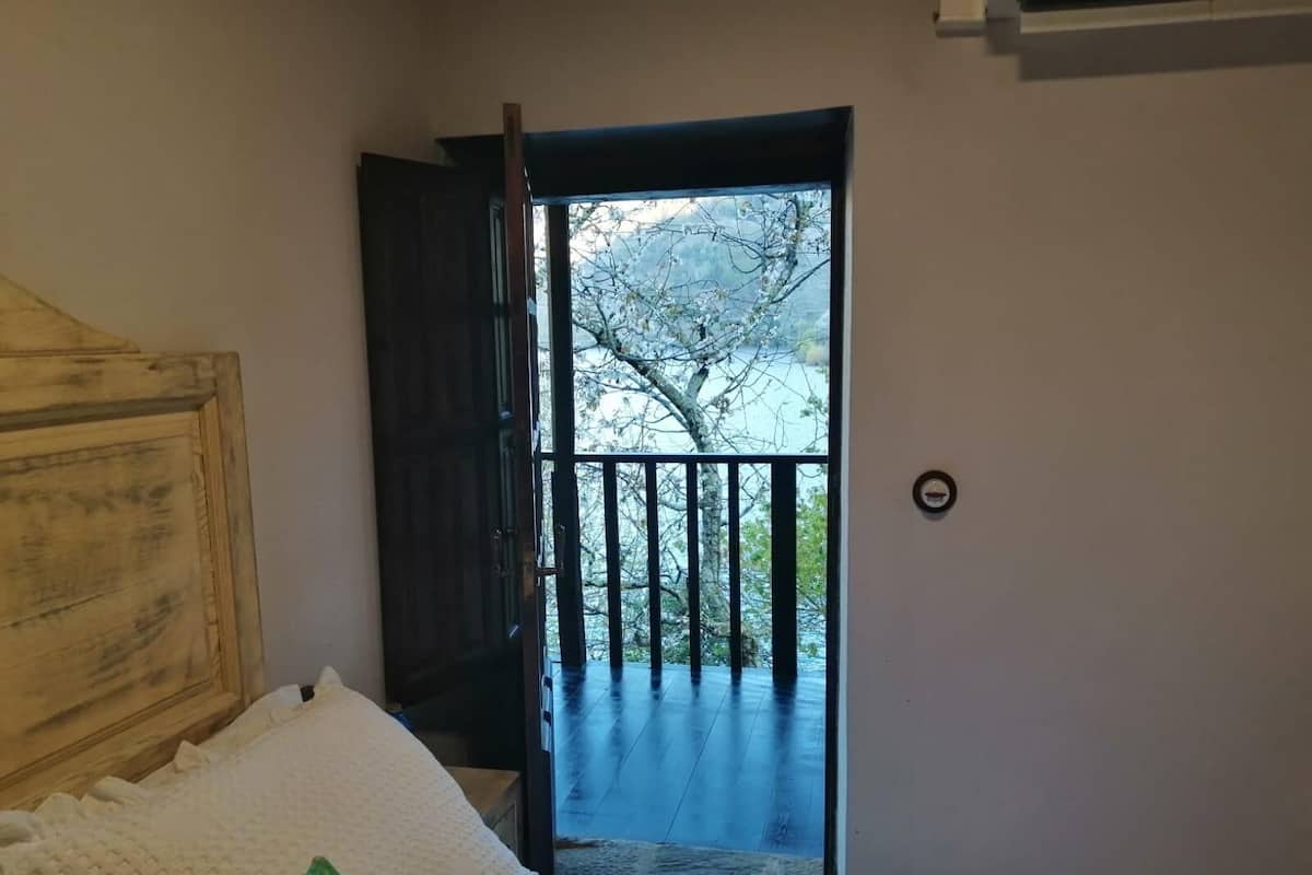 A bedroom with a bed, a wooden headboard, a window with a view of trees, and a door leading to an outdoor balcony.