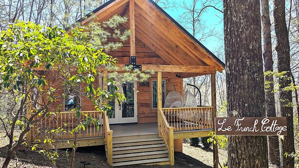 A wooden cabin with a porch, surrounded by trees.