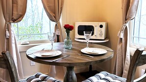 A dining table with chairs, a vase with red flowers, and a microwave on the wall.