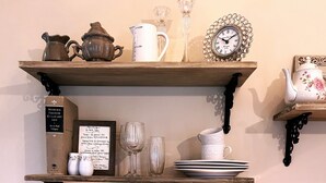 A wooden shelf with kitchenware, a framed menu, and a table lamp.