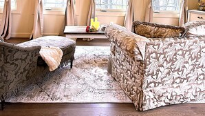 A spacious room with a large window, a sofa, a chair, and a small table with candles.