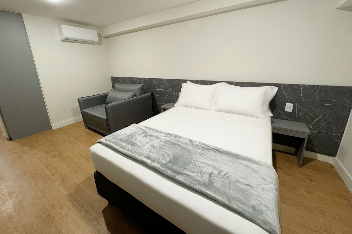 Ein modernes Schlafzimmer mit Bett, Stuhl, Nachttisch und Klimaanlage.
