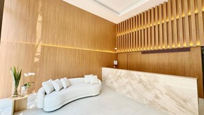 Una moderna zona de recepción con un sofá blanco curvo, paneles de madera y un mostrador de mármol.
