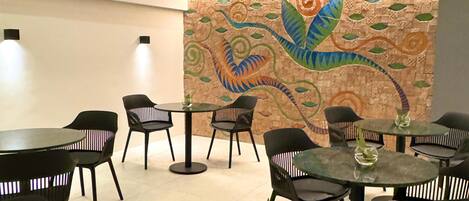 Un interior moderno con mesas redondas y sillas negras, una pared decorativa con un mosaico y un techo con diseño perforado.