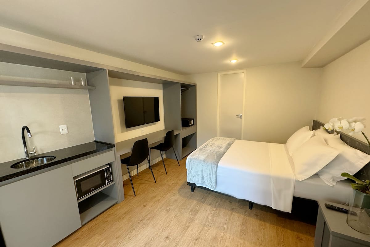 Ein kleines Hotelzimmer mit Küchenzeile, einem Bett, einem Schreibtisch und einem Fernseher.