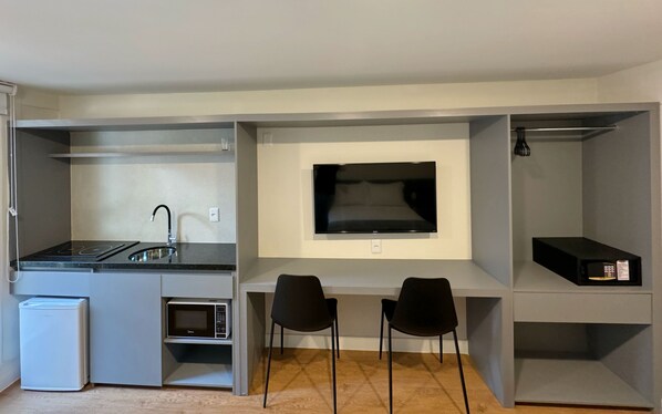 A compact kitchenette with a stove, sink, and microwave. There are two black chairs and a flat-screen TV mounted on the wall.