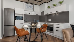 A modern kitchen with white cabinetry, a stainless steel refrigerator, a built-in oven, and a dining area with two chairs and a table. - Luxury Century City Apartment | Lagoon Views (Cape Town)
