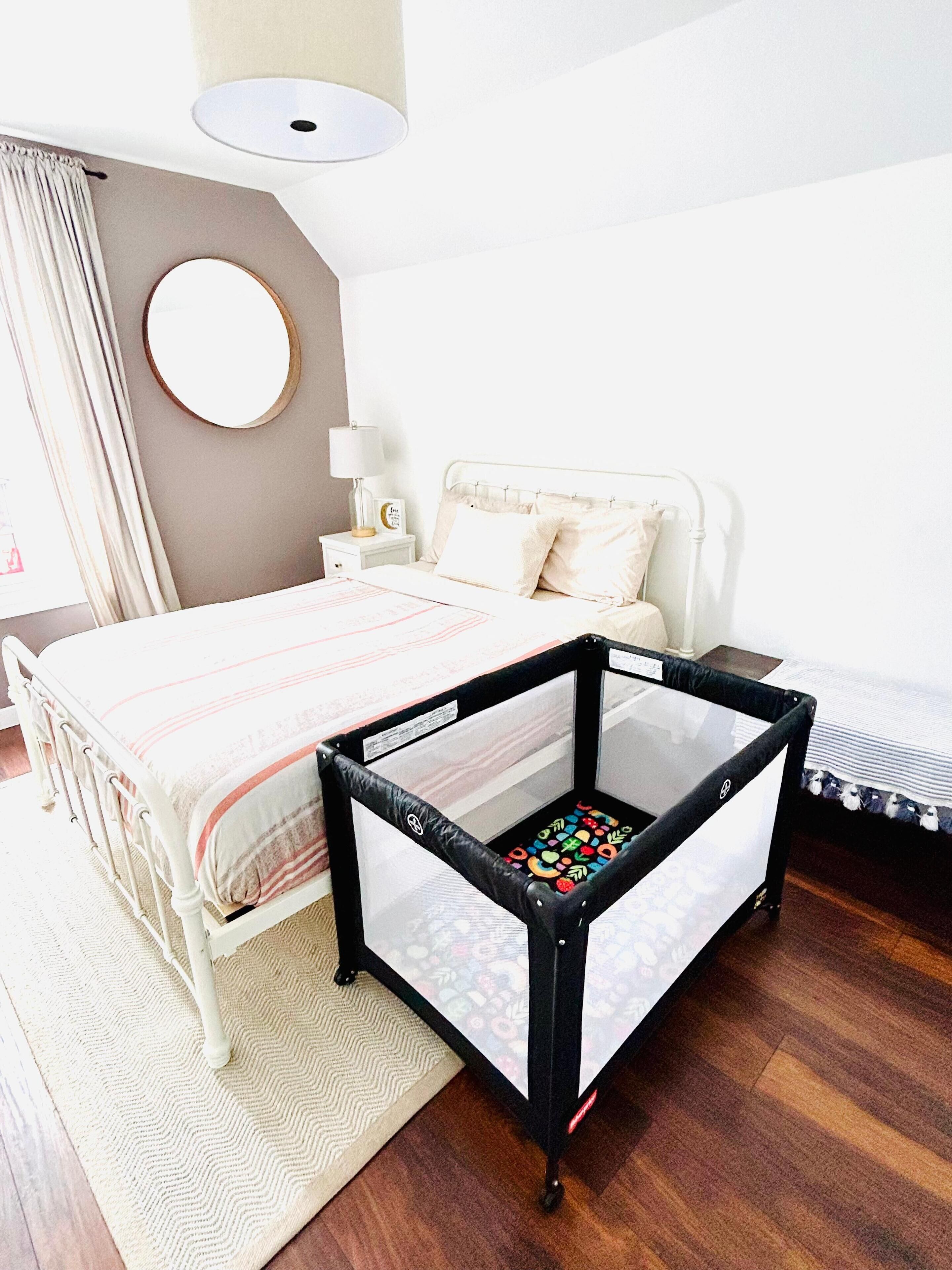 Une chambre à coucher avec un lit, une table de chevet, une lampe, un miroir et un parc pour bébé.