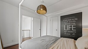 Een slaapkamer met een bed, een hanglamp en een motiverende quote op de muur.