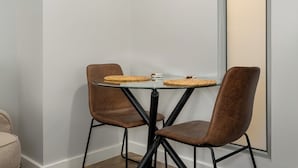 A glass-top table with woven placemats and two brown upholstered chairs. - Foreshore Place | Modern Studio | Netflix (Cape Town)
