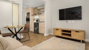 A modern living room with a sofa, a glass-top coffee table, a TV mounted on the wall, and a wooden cabinet. - Foreshore Place | Modern Studio | Netflix (Cape Town)