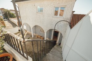 A residential building with a staircase leading to a balcony, a small window, and a door.