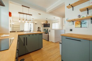 Een moderne keuken met grijze kastjes, houten aanrechtblad en hangende lampen.
