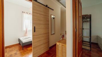 A bedroom with a bed, a wooden wardrobe, a mirror, and a wooden floor.