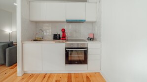 A compact kitchen with white cabinets, a built-in oven, a coffee maker, and a microwave. - Downtown Sunny Apartment by Vacationy (Porto)