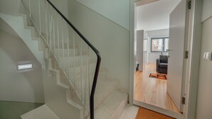 A modern staircase with glass railings and a wooden floor leading to a room with a grey sofa and a window. - Downtown Sunny Apartment by Vacationy (Porto)