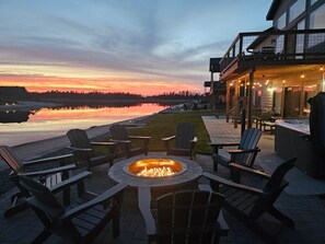 An outdoor seating area with Adirondack chairs and a fire pit, overlooking a body of water and a building with outdoor lighting. - Sunset Serenity at Castle Rock (New Lisbon)