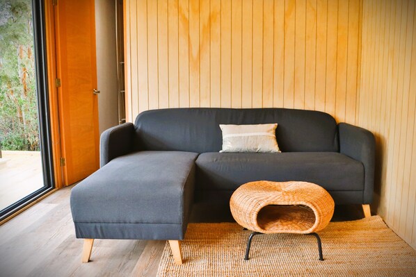 Una sala de estar moderna con un sofá modular, un pouf tejido y un ventanal grande.