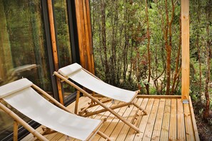 Una terraza de madera con dos sillones blancos que dan a una vista del bosque a través de amplios ventanales.
