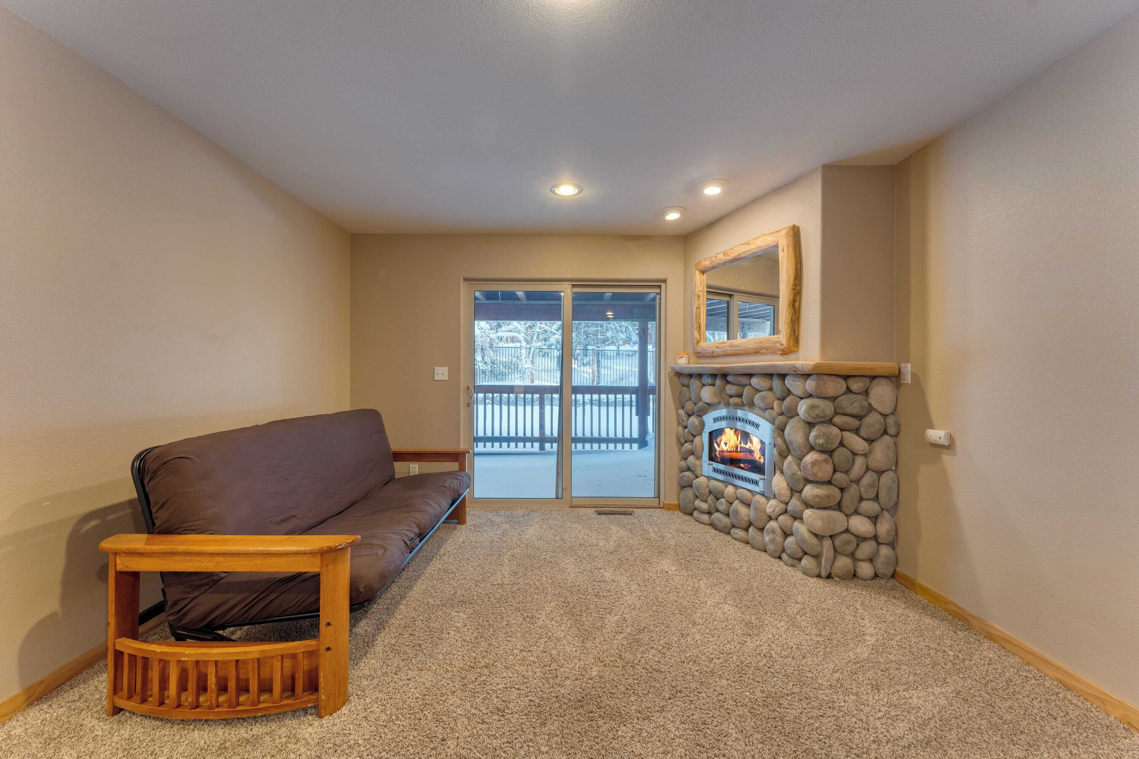 A living room with a brown sofa, a small wooden table, a stone fireplace, and a large sliding glass door leading to a balcony.