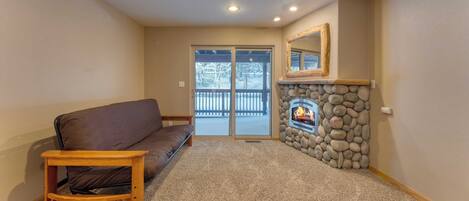 A living room with a brown sofa, a small wooden table, a stone fireplace, and a large sliding glass door leading to a balcony.