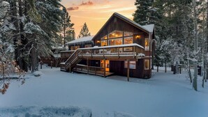 A wooden lodge with a balcony and stairs, surrounded by snow-covered trees.