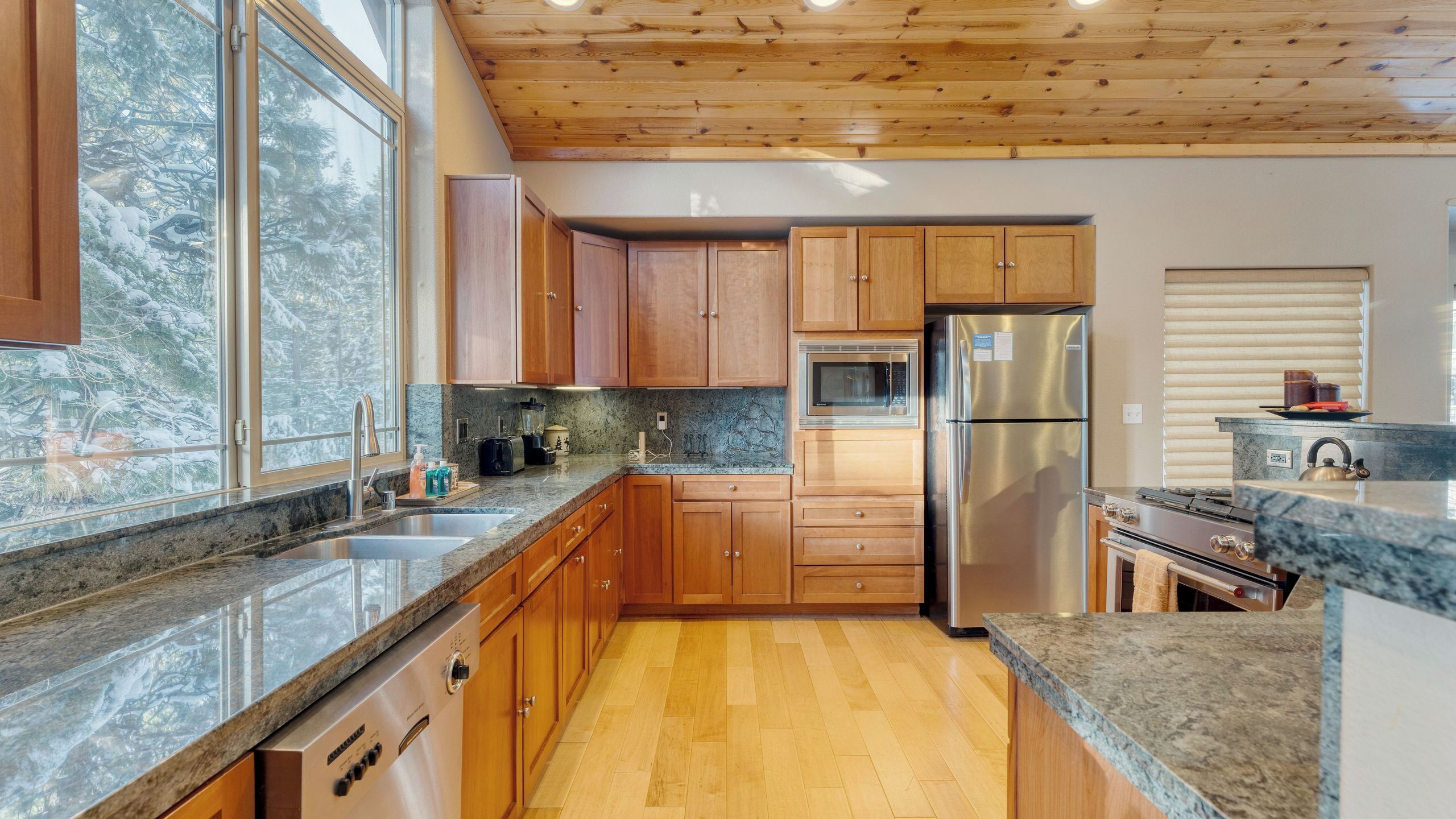 Una cocina con gabinetes de madera, un refrigerador de acero inoxidable, horno empotrado y encimera de granito.