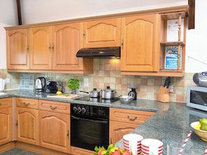 A kitchen with wooden cabinets, a stove, a microwave, and a coffee maker. - Miller's Cottage -UK48595 (Warbstow)