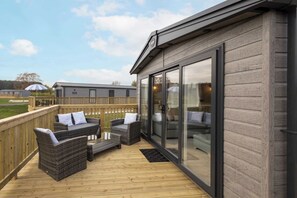 A covered outdoor area with wicker furniture and a wooden deck. - Host & Stay | Fieldview Lodge, Ashdown Retreat (Pickering)