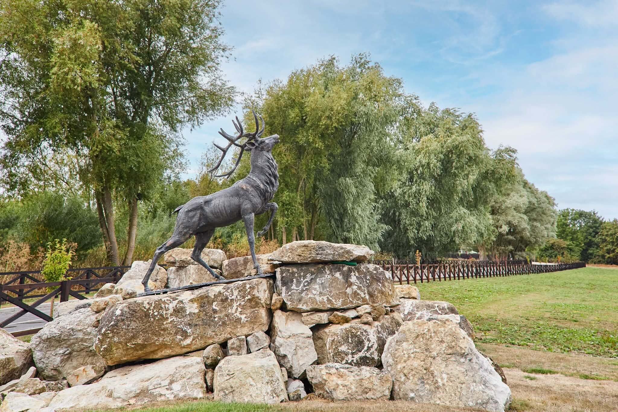 A deer statue on a rock formation with a wooden fence and trees in the background.