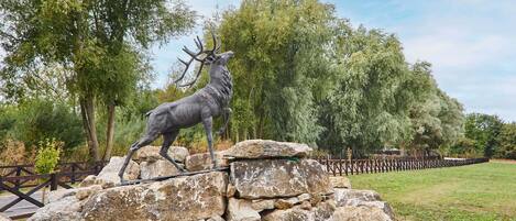 A deer statue on a rock formation with a wooden fence and trees in the background.