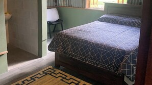 A bedroom with a bed, a chair, a window, and a bathroom.