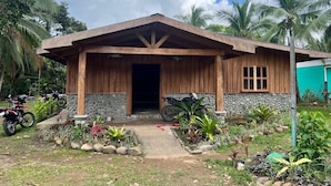 A wooden house with a stone facade, a porch, and a garden with tropical plants.