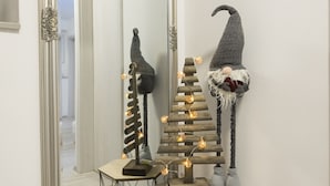 Un couloir avec un miroir, une statuette de gnome et un arbre décoratif illuminé.