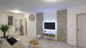 Un salon moderne avec un téléviseur à écran plat fixé à un mur en pierre, une petite table ronde, un canapé et une plante en pot.
