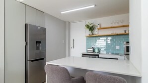 A modern kitchen with a stainless steel refrigerator, a white countertop, and two grey chairs.
