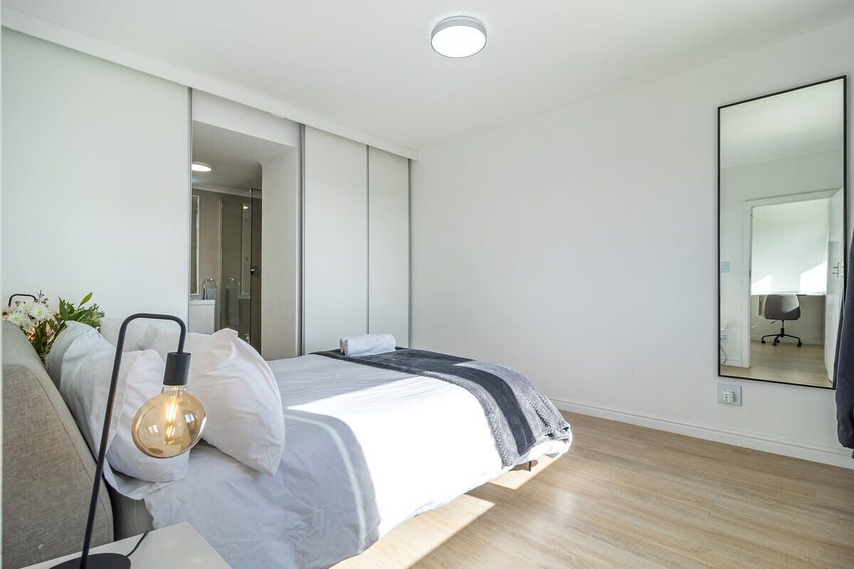 A modern bedroom with a bed, bedside lamp, and a large mirror.