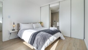 A modern bedroom with a bed, bedside table, lamp, and a large mirror.