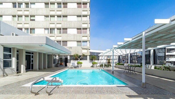 A swimming pool with a clear blue water, surrounded by a covered area with chairs and potted plants.