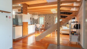 Amplia sala de estar con una escalera de madera, una cocina con refrigerador moderno y una pared de acento de piedra.