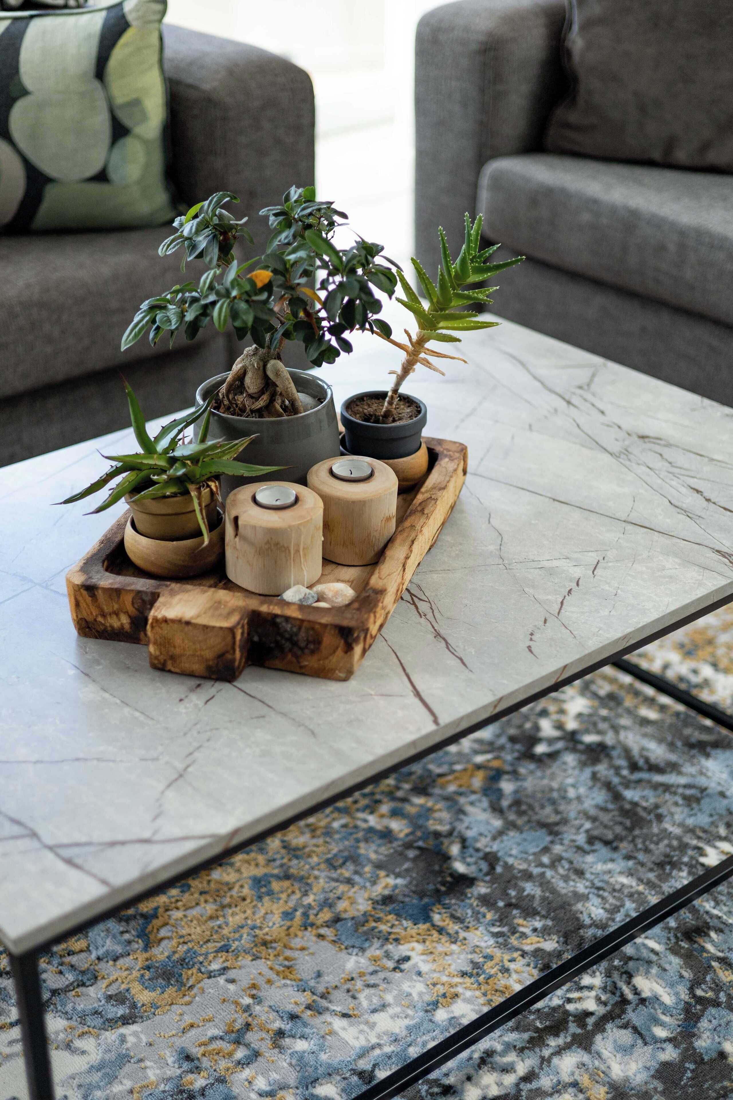 Un salon avec une table basse en marbre, un canapé gris et un tapis à motifs.